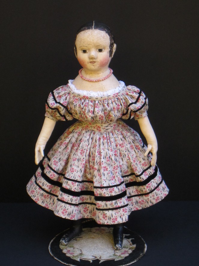Her dress made from antique pink and black print fabric is adorned with rows ans rows of black velvet ribbon.